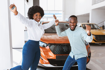 Excited Afro couple gesturing YES, celebrating successful car purchase, dancing and having fun at...
