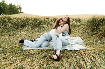 Naklejka na ściany i meble cute girls are sitting in the field on a picnic. beautiful sisters of different ages. portrait of girlfriends