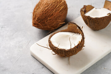 Cracked and whole coconuts on marble board on grey concrete surface, copy space