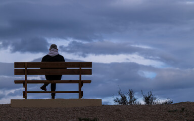 Rear view of man sitting on bench against cloudy Sky. Almeria, Spain