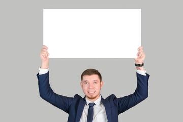 A businessman in formal attire holds a rectangular white poster