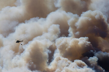 A fire helicopter with a bambi bucket in the clouds of a forest fire