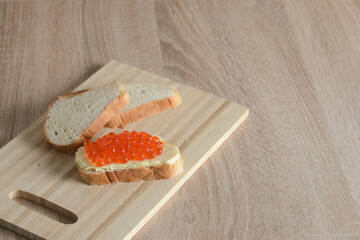 Sandwich with butter and red caviar on a cutting board with slices of white bread.