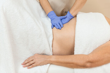 Side view of a physiotherapist checking diastasis recti on belly of mature woman