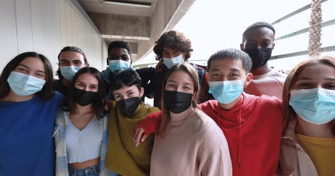 Multiracial young friends having fun smiling on camera outdoor while wearing safety face masks for coronavirus outbreak - Colle university and social distance concept