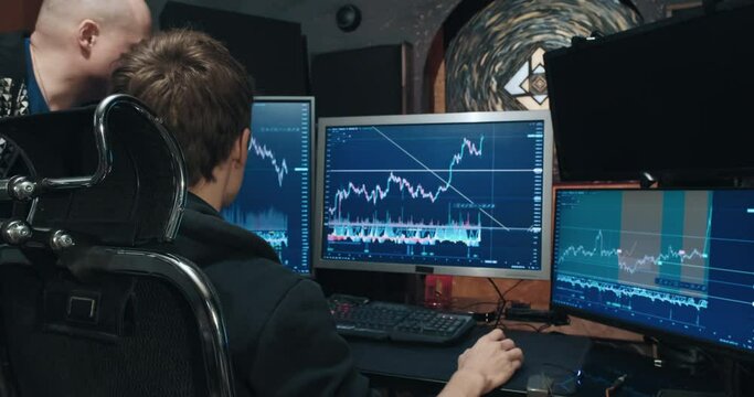 Two male traders on stock exchange, discussing charts of falling and rising quotes on the monitor screen, home environment, freelance. Concept of playing on stock, futures and bonds trading exchange