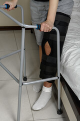 Woman wearing leg brace after surgery on knee fracture trying to walk with walker. Rehabilitation...