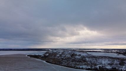 Fototapeta premium Flying over a snowy field. The city dump is visible, covered with snow. Mothballed waste landfill. Aerial photography.