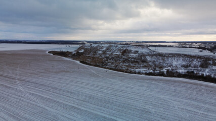 Flying over a snowy field. The city dump is visible, covered with snow. Mothballed waste landfill. Aerial photography.