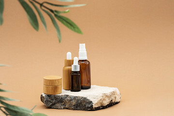 Fototapeta na wymiar Blank amber glass and bamboo essential oil bottles with pipette, glass spray bottle and bamboo jar on natural stone podium. Organic spa cosmetic beauty product mock up.