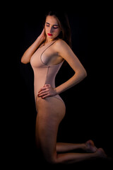 Girl in a beige bodysuit on a black background.