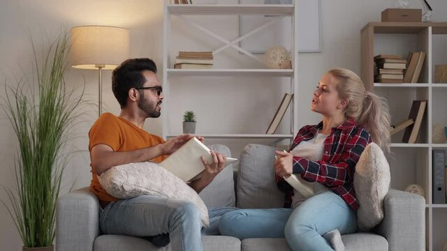 Study language. Couple student. Homework help. Casual man and woman discussing information in books sitting sofa in light room interior.
