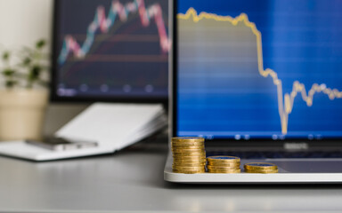 Stacks of coins in the form of a decline chart on the background of computer monitors. The concept of loss and fall in value. Selective focus on coins