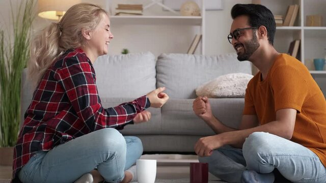 Meeting friends. Diverse couple. Enjoying fun. Happy casual man and woman playing game rock-paper-scissors sitting light room interior.