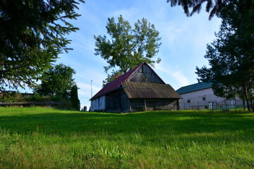 Obraz premium A close up on an old abandoned wooden house located in the middle of a forest or moor next to some trees, a well and a fence, spotted on a sunny summer day during a hike on a Polish countryside