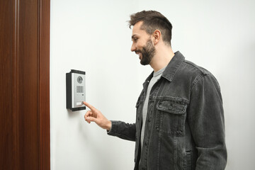 Happy man ringing intercom with camera in entryway