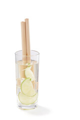 A transparent cocktail with ice cubes and slices of lime is contained in a high glass with reusable bamboo straws. The glass is isolated on the white background.