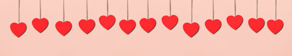 Bright red heart-shaped cards hanging on strings on a light peachy background