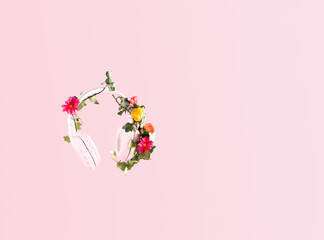 Headphones against pastel pink background. Floral decoration, nature minimal concept. Springtime, leisure, holidays. 