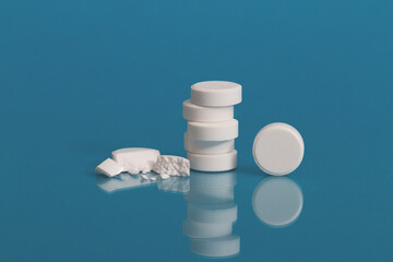 A column of pharmaceutical white pills on a bright blue background is reflected on a glass surface. one pill is broken.Medicine concept. Minimalist style. Trendy colors. Isolated.