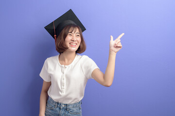 Portrait of young Asian student wearing graduation cap over studio background.