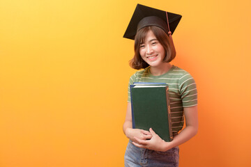 Portrait of young Asian student wearing graduation cap over studio background.