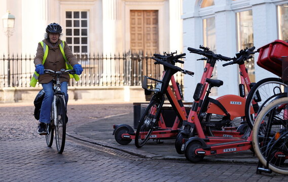 A woman cycles past parked up electric scooters in Cambridge