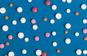 Many multi-colored pills on a blue background as a prescription treatment concept. Varieties of painkillers and antibiotics, allergies to drugs. Close-up.