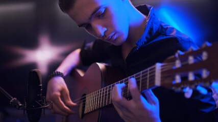 Naklejka premium Man plays guitar. Young man plays a musical instrument. Musician records his composition in a music Studio using professional microphone