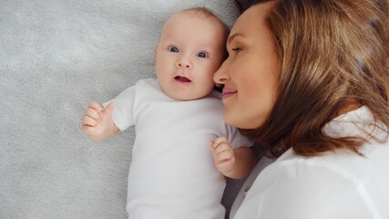 Happy newborn baby with his mother. Healthy newborn baby in a white t-shirt with mom. Closeup Faces of the mother and infant baby. Cute Infant boy and parent, top view. Happy family portrait