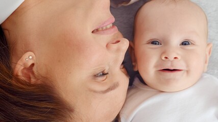 Happy newborn baby with his mother. Healthy newborn baby in a white t-shirt with mom. Closeup Faces of the mother and infant baby. Cute Infant boy and parent, top view. Happy family portrait