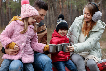 Happy family with cups of hot tea spending time together in forest