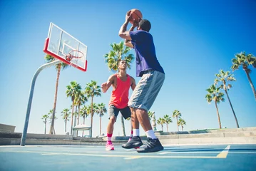 Fotobehang Young players playing basketball at the court in venice beach, California. Professional street ballers having fun performing tricks and huge slam dunks © oneinchpunch