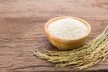 Organic white rice or jasmine rice in a wooden bowl with the ears of rice lying on the wooden floor