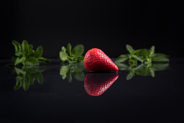 Una fresa entera aislada sobre agua con hojas de menta. Reflejo espejo sobre agua y fondo negro
