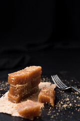 Dulce pasta de gelatina de membrillo dorado con sésamo molido y un tenedor sobre una placa de madera negra	