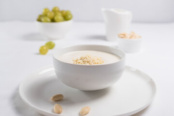 Obraz na płótnie Canvas Crema de almendras, sopa fría española. Ajo blanco de Málaga con almendras y uvas en un recipiente blanco sobre una mesa blanca 