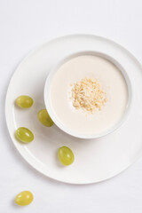 Crema de almendras, sopa fría española. Ajo blanco de Málaga con almendras y uvas en un recipiente blanco sobre una mesa blanca. Vista superior