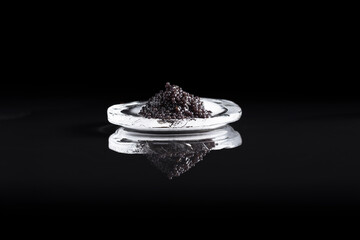 Caviar negro de esturión sobre una piedra de hielo reflejada en fondo negro. Comida delicatessen de lujo	