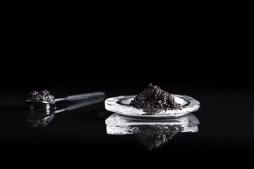 Caviar negro de esturión en una cuchara, sobre una piedra de hielo reflejada en fondo negro. Comida delicatessen de lujo	