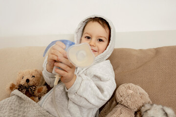 Sick little boy with inhaler for cough treatment. Unwell kid doing inhalation on his bed. Flu...