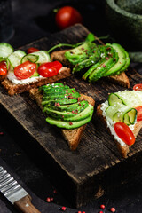 Toast with cream cheese, avocado, cucumber and tomato on a table