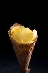 Patatas fritas saladas en un cono de papel. Aperitivo en sobre fondo oscuro	