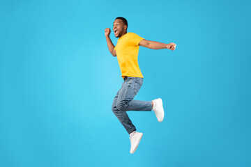 Joyful African Man Jumping And Shouting In Mid-Air, Blue Background