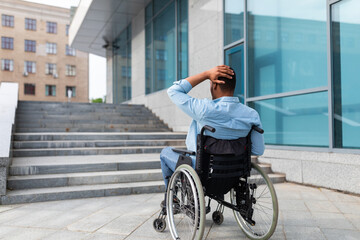 Irritated impaired black man in wheelchair having no possibility to enter building without ramp, outdoors - obrazy, fototapety, plakaty