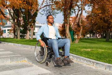 Paraplegic black guy in wheelchair going down ramp on on walk at park in autumn, using impaired...