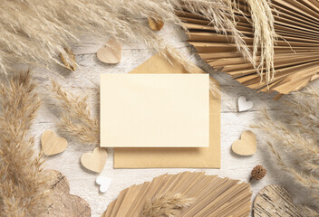 Blank card and envelope on white wooden table near dried pampas grass and hearts, Boho mockup