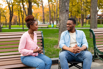 Cheerful disabled black guy in wheelchair having conversation with his girlfriend at park in autumn