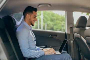 Young arab man CEO working at car backseat, using laptop