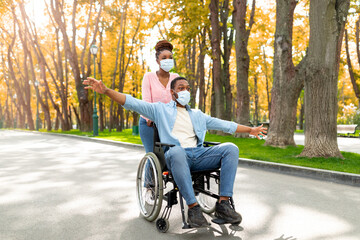 Young Afro woman on walk with her paraplegic boyfriend in wheelchair during covid outbreak at autumn park